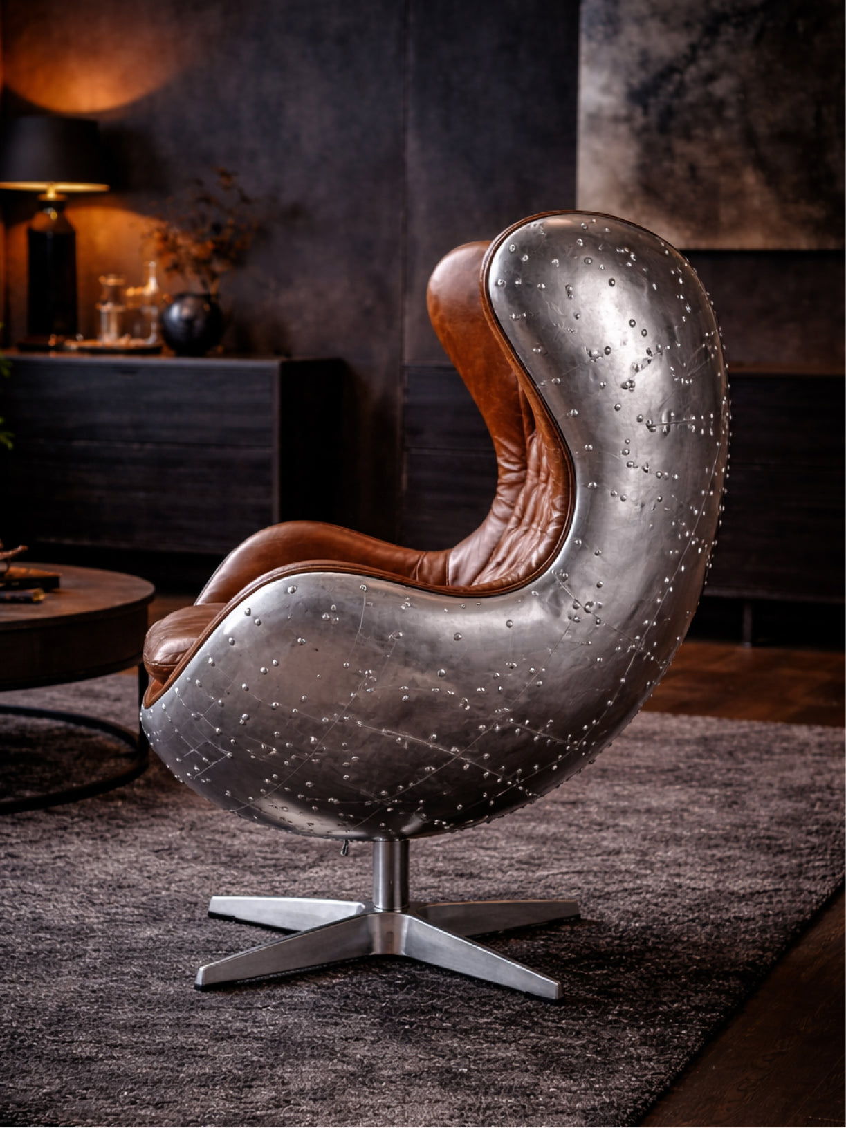Seitenansicht: Möbelloft Hudson River Aviator Sessel mit cognacfarbenem Leder und genietetem Aluminium in modernem, dunklem Wohn-Setting