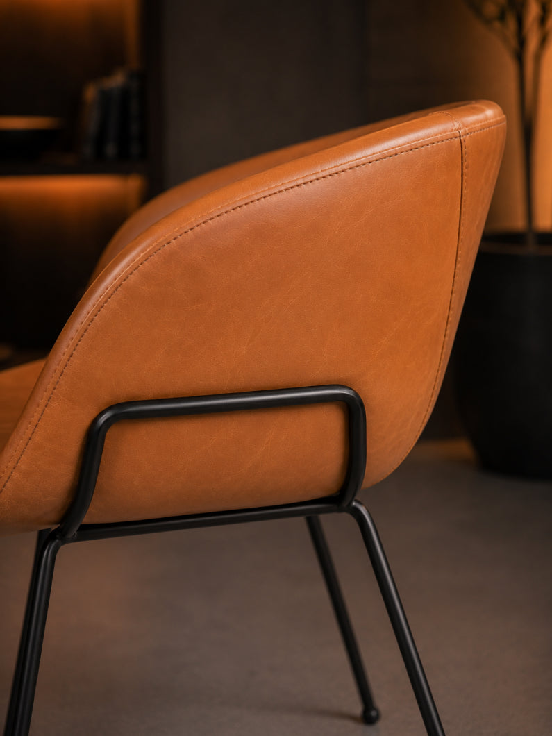 Nahaufnahme des Design Stuhl Monkey mit cognacfarbenem Bezug, sanft gerundeter Rückenlehne und schwarzem Stahlgestell